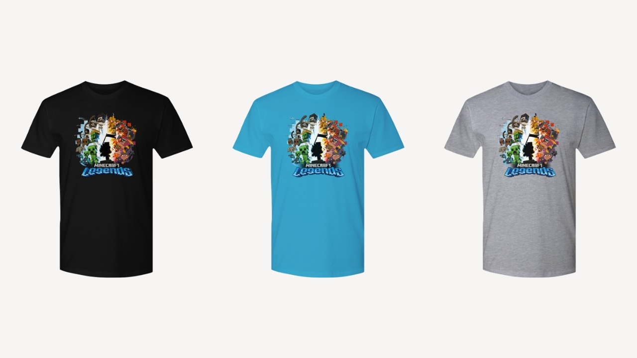 An image of three T-shirts side by side, each a different color (black, blue, and grey respectively) featuring key art from Minecraft Legends